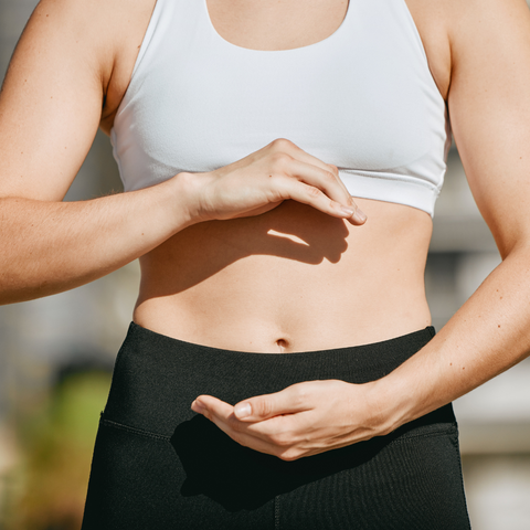 Woman in workout clothes framing her stomach with both hands outdoors