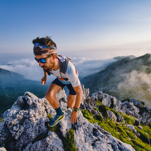 Trail runner scrambling up a rocky mountain ridge above the clouds