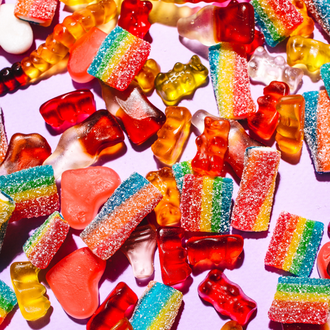Assorted gummy bears and sour candy strips scattered on a lilac background