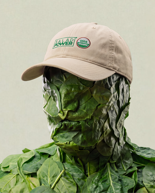Figure covered in spinach leaves wearing an ecru SaladPower cap