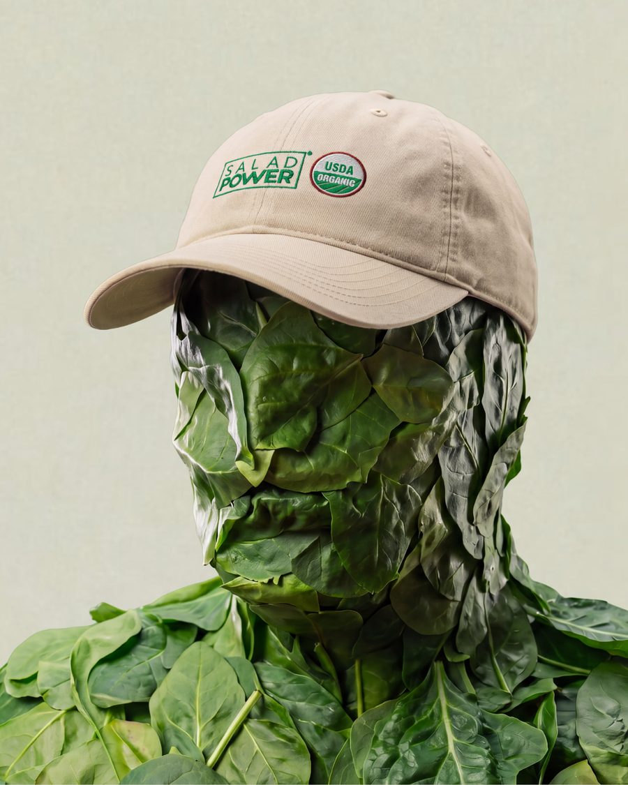 Figure covered in spinach leaves wearing an ecru SaladPower cap
